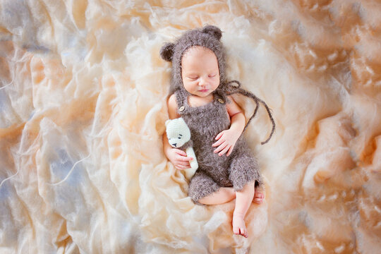 New born sleeping baby in a bear costume and holding a toy. Beautiful posing of a newborn baby in a hat with ears and overalls.