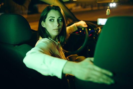 Young woman drives car in a reverse at night.