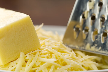 Cheese and grated cheese on a metal grater, close-up. blurred background