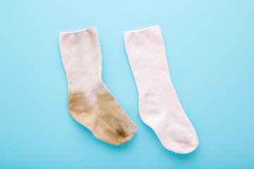 Compare between dirty and clean baby socks on light blue table background. Pastel color. Closeup. Top down view.