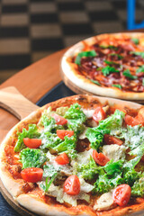 Caesar pizza served on a wooden table over blurred background in restaurant. Italian pizza with caesar salad filling.