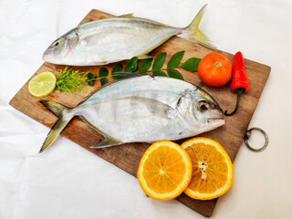 Fresh Malabar Trevally fish decorated with herbs and fruits on a wooden pad ,Isolated on white Background.Selective focus.