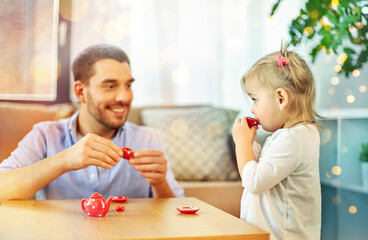 family, fatherhood and childhood concept - happy father and little daughter with toy crockery playing tea party at home
