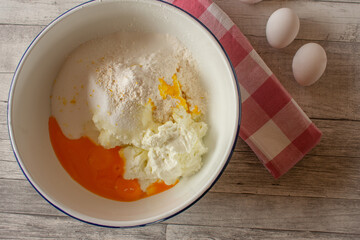 Ingredients for a cheese cake filling in a white enamel bowl from above