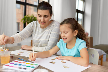 family, hobby and leisure concept - happy smiling mother spending time with her little daughter drawing or painting wooden chipboard items with colors at home