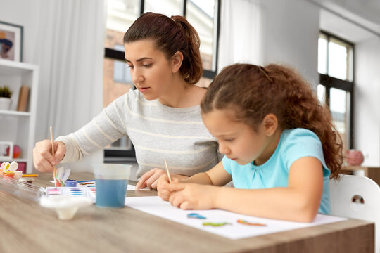 family, motherhood and leisure concept - mother spending time with her little daughter drawing or painting wooden chipboard items with colors at home