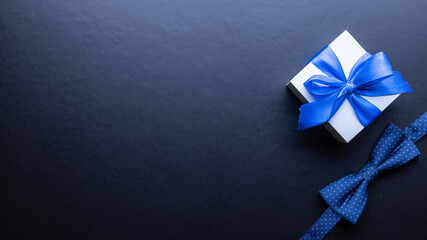 Gift father day. Blue bowtie or tie, white box with bow ribbon on dark background. Happy loving family and Fathers Day concept.