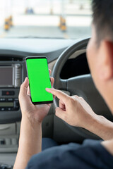 Mock up of man using mobile smart phone inside a car. Driver hand holding blank green screen smartphone, searching address and pin location via map navigator application, transportation