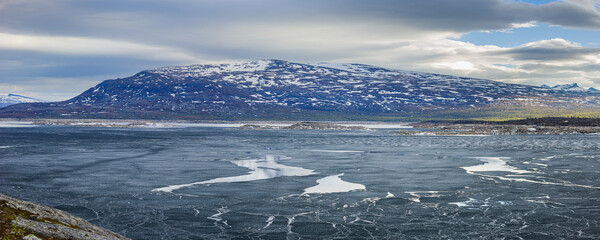 Panoramic image of a landscape in spring with the half frozen reservoir Akkajaure and mountains in Sarek National Park under overcast sky, Lapland, Sweden.