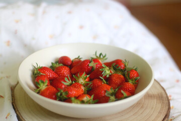 Bowl of fresh strawberries and wooden tray on a bed. Selective focus.