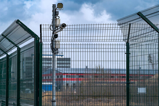 A metal lattice fence and security cameras guard the area. Fence, great design for any purpose. The concept of safety of industrial territories.