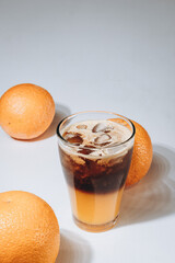 a glass of a double portion of coffee with fresh orange photographed on a solid background with whole oranges