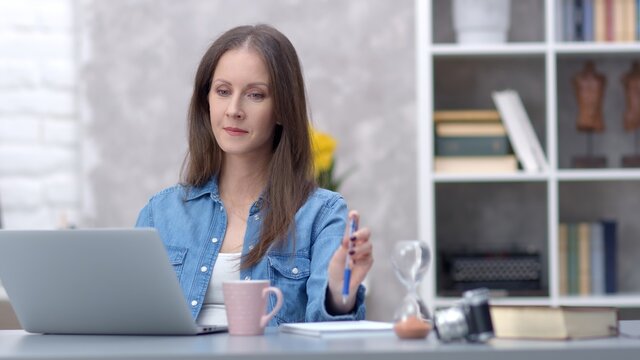 Young woman working online with laptop computer at home sitting at desk. Businesswoman in home office, browsing internet.