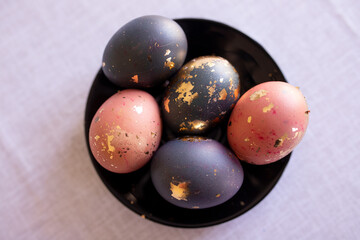 homemade colored Easter eggs with gols ornaments on a plate against a gray linen tablecloth...
