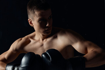 muscular boxer in black gloves on a dark background looking to the side cropped view