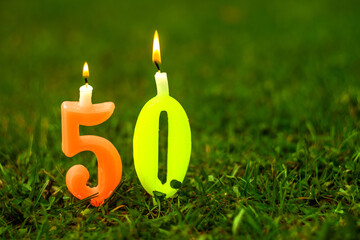 The numbers 50 from burning candles on a green summer background, a photo for a greeting collage.