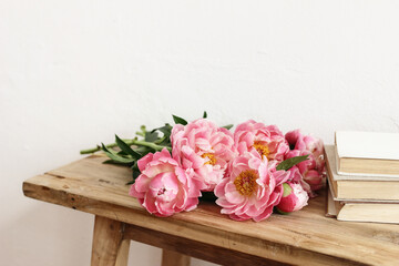 Close-up of pink peonies flowers, bouquet and books. lying on old wooden table. White wall. Selective focus, blurred background. Wedding or birthday celeberation concept. Floral still life scene. - Powered by Adobe