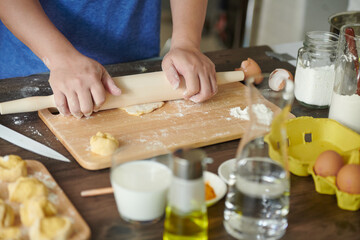 Female hands roll out a piece of dough with a rolling pin for making ravioli or dumplings on a wooden table sprinkled with flour. A step-by-step recipe for cooking ravioli or dumplings
