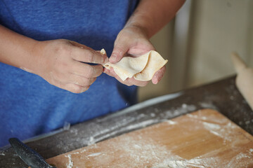 Front view of woman's hands making meat dumpling with wooden rolling pin. The process of making homemade dumplings. Minced meat on dough, the process of cooking Italian ravioli. Russian food.