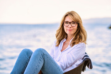 Attractive mature woman wearing white shirt and blue jeans while relaxing by the sea