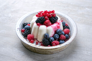 Modern style traditional blancmange almond pudding with wild berry coulis served as close-up in a...