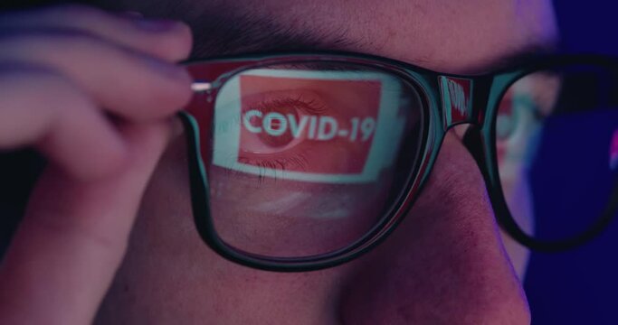 Close-up portrait of man in eyeglasses late at night scrolling news abous coronavirus in front of laptop, macro shot