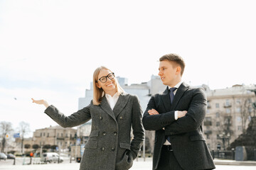 Businessman and businesswoman in office suits in the city. Girl holding a hand shows the city. Successful and confident office workers.