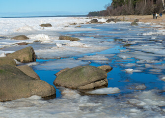 winter landscape by the sea, ice and stones in the dune area, in the distance the sea horizon, blue sky