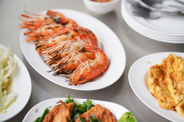 Grilled shrimp. Many dishes served on the table including Thai style omelette, stir fry cabbage and fish cakes. Soft focus on the prawn.