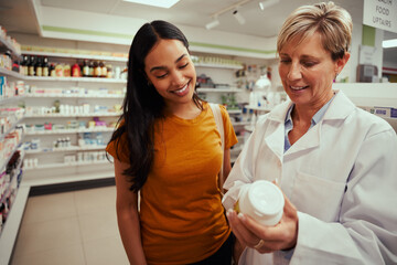Senior pharmacy woman helping female customer find bottle of medicine from shelves