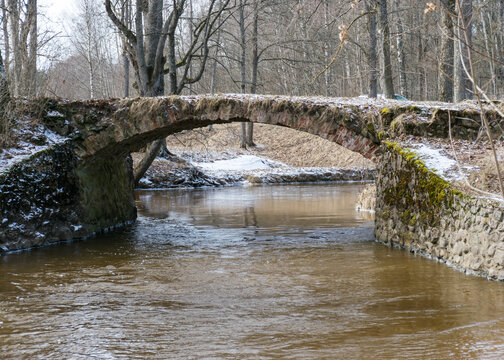 a continuous boulder stone bridge with a brick used for masonry, early spring, bare trees, snow plan on the ground, Stone arch bridge over the river Kuja, Madona, Latvia