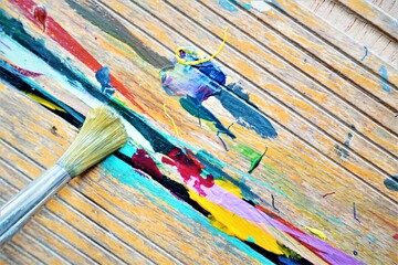 Painted wood surface with one paintbrush.  Brush bristles with paint and colorful streaks on...