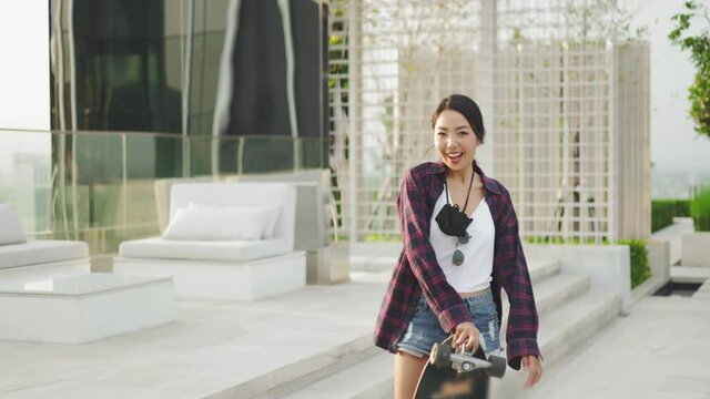 Attractive Asian woman smiling  play skateboard outdoor garden.she holding surf skate.Happy young   people play surf skate at park city.