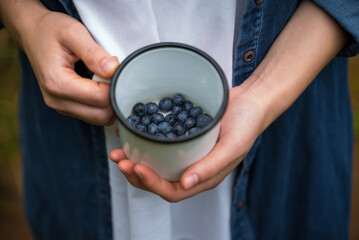 Girl holding a mug with fresh blueberries in nature