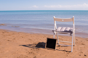 a white chair stands on the seashore, next to it is an empty black plaque in a frame