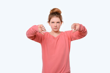 Fototapeta premium Portrait of a cute young girl in pink casual sweatshirt showing thumbs down. White background