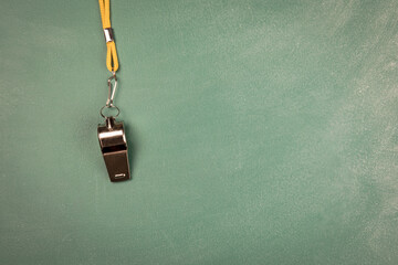Fototapeta na wymiar Metal whistle with yellow cord on a green chalk board