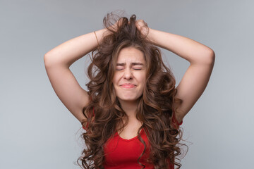 Anxious and troubled young brunette woman grab head with hands, close eyes, standing over gray background