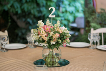 Centerpiece made of pink and white flowers stands in the middle of festive dinner table.