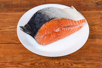 Piece of uncooked salmon on white dish on rustic table