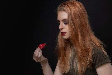 Low key portrait of beautiful long hair young woman posing with fresh strawberry. Horizontally. 