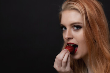 Portrait of attractive  long hair young woman tasting fresh strawberry looking at the camera. Horizontally. 