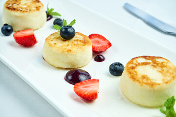 An ideal breakfast - Cottage cheese pancakes with sour cream, berry sauce, strawberries, blueberries in a white plate on a white tablecloth. Ukrainian syrniki