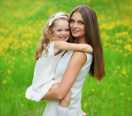 Fototapeta premium Portrait of happy smiling mother with little girl child on the grass in a summer park