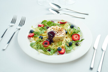 Grilled camembert cheese with apples, strawberries and blueberries in a white plate on a white plate. Close up, selective focus