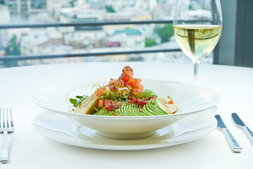 A delicious and healthy salad with artichokes, avocado, tuna and quinoa, served in a white plate on a white tablecloth. Restaurant food service