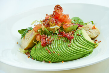 A delicious and healthy salad with artichokes, avocado, tuna and quinoa, served in a white plate on a white tablecloth. Restaurant food service