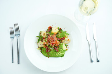 A delicious and healthy salad with artichokes, avocado, tuna and quinoa, served in a white plate on a white tablecloth. Restaurant food service
