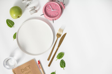 Composition with cutlery, empty plate, measuring tape, diet plan, apple and alarm clock on white...