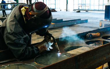 Craftsman welding steel structure cellular beam with sparks fly from gas machine in fabrication factory.